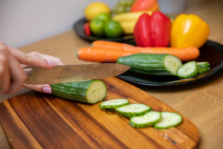 hands-slicing-a-cucumber-on-a-wooden-cutting-board